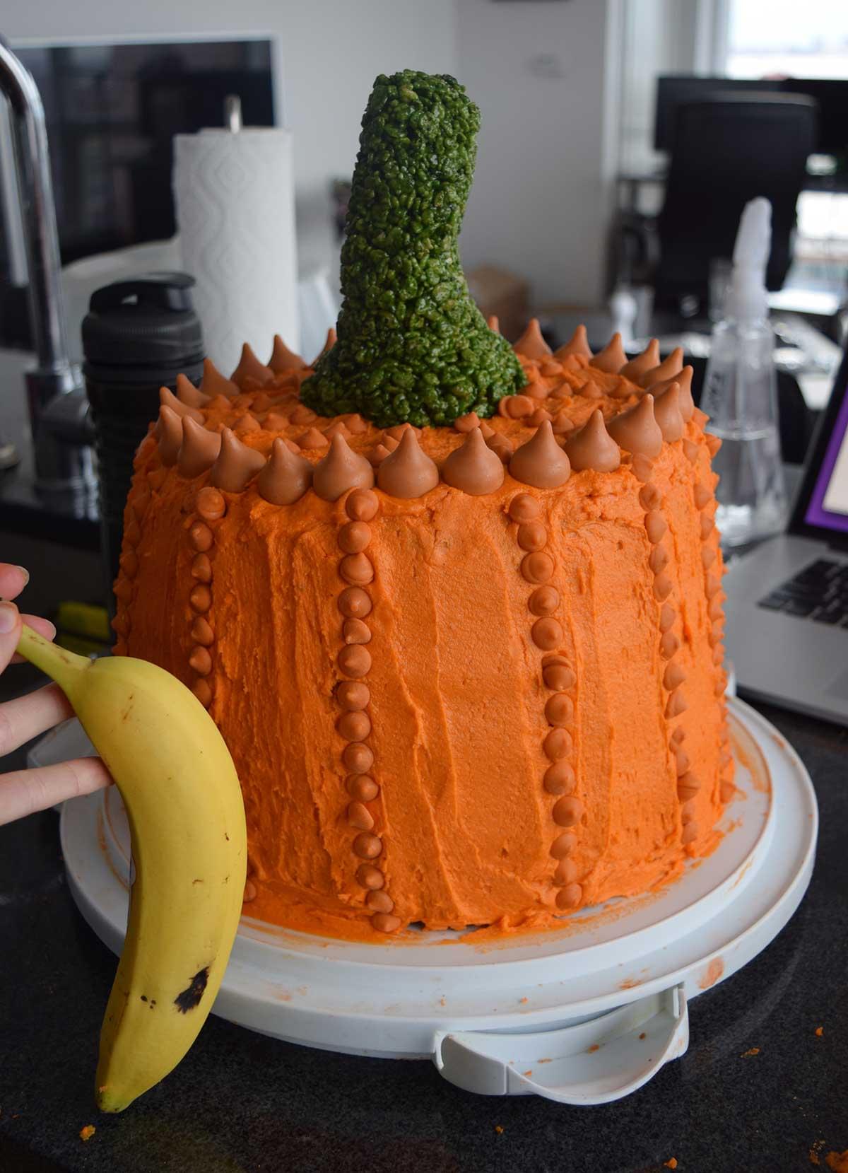 Large cake decorated to look like a pumpkin, with small banana shown for scale.