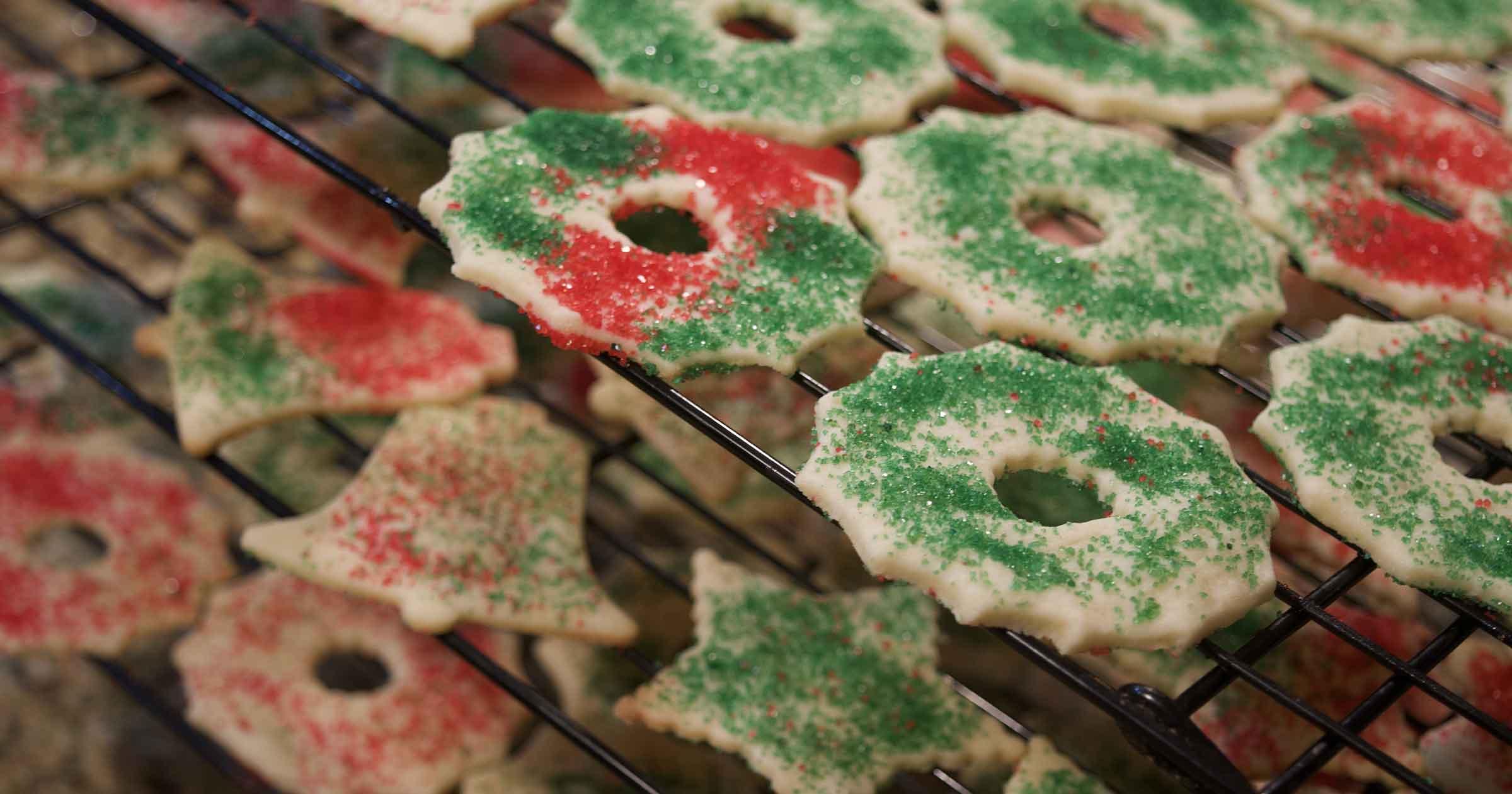Stacked cooling racks full of wreath, star, and bell-shaped sugar cookies