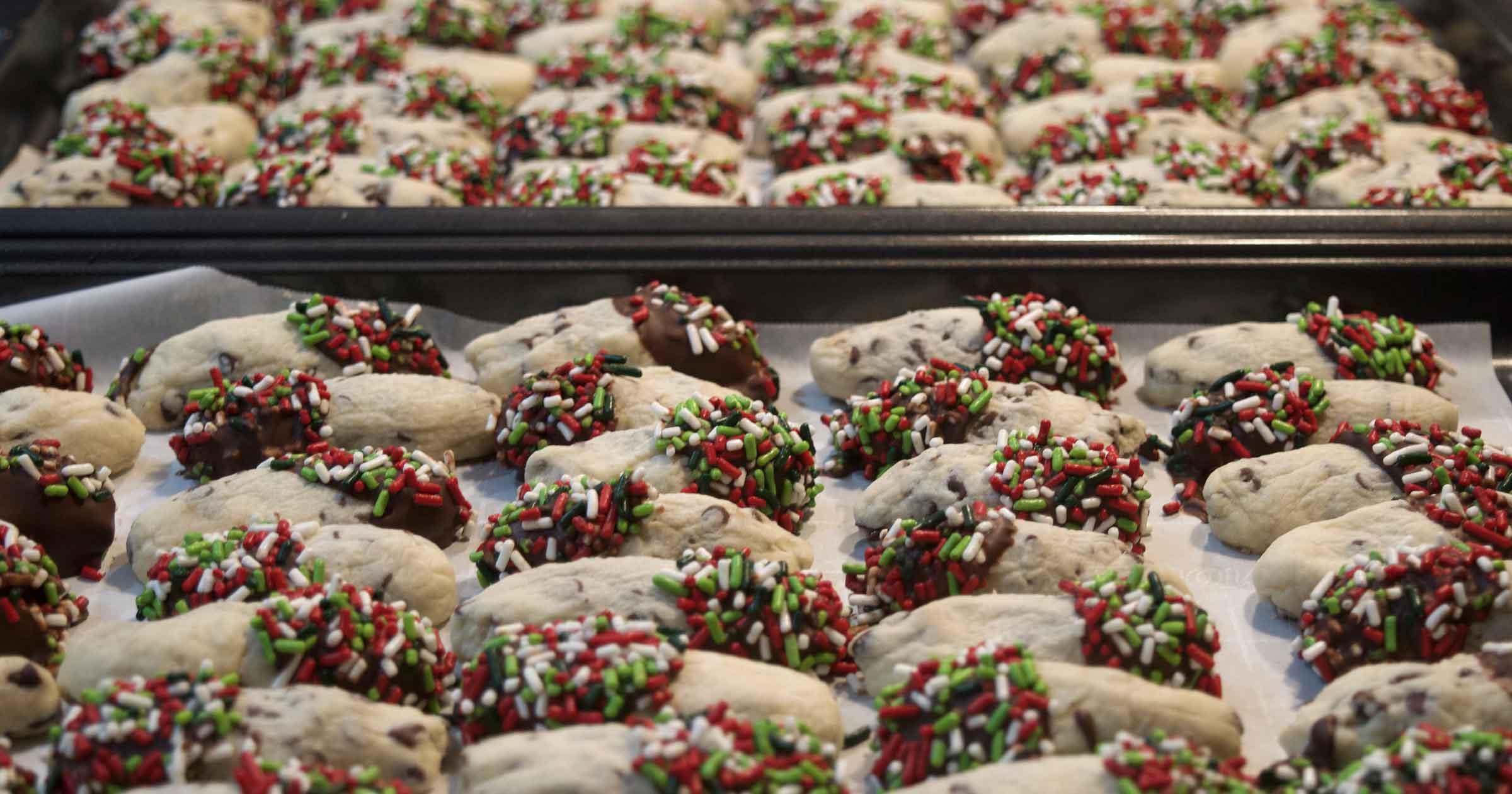Baking sheets packed with chocolate-dipped chocolate chip cookies with holiday sprinkles